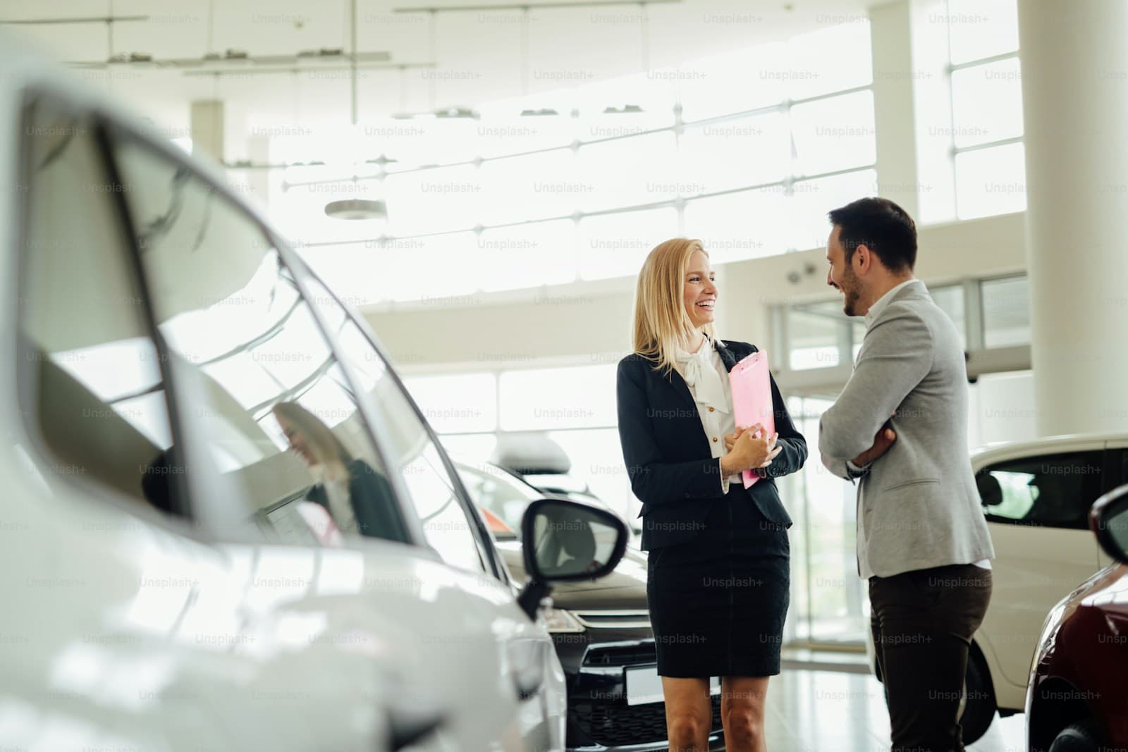 Two professionals talking in a bright dealership showroom surrounded by new cars