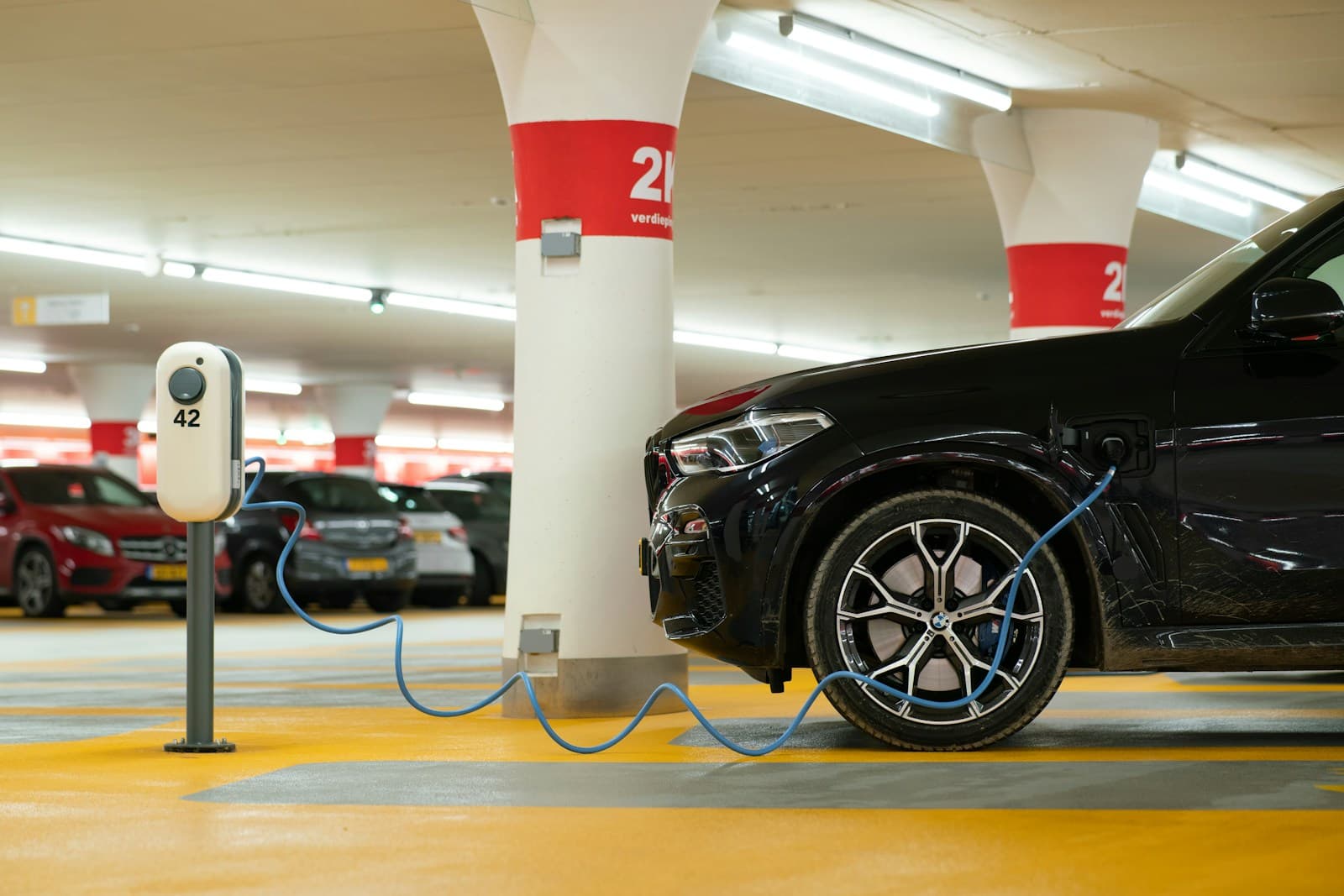 Black electric car charging at EV station in underground parking garage with numbered pillars and bright lighting